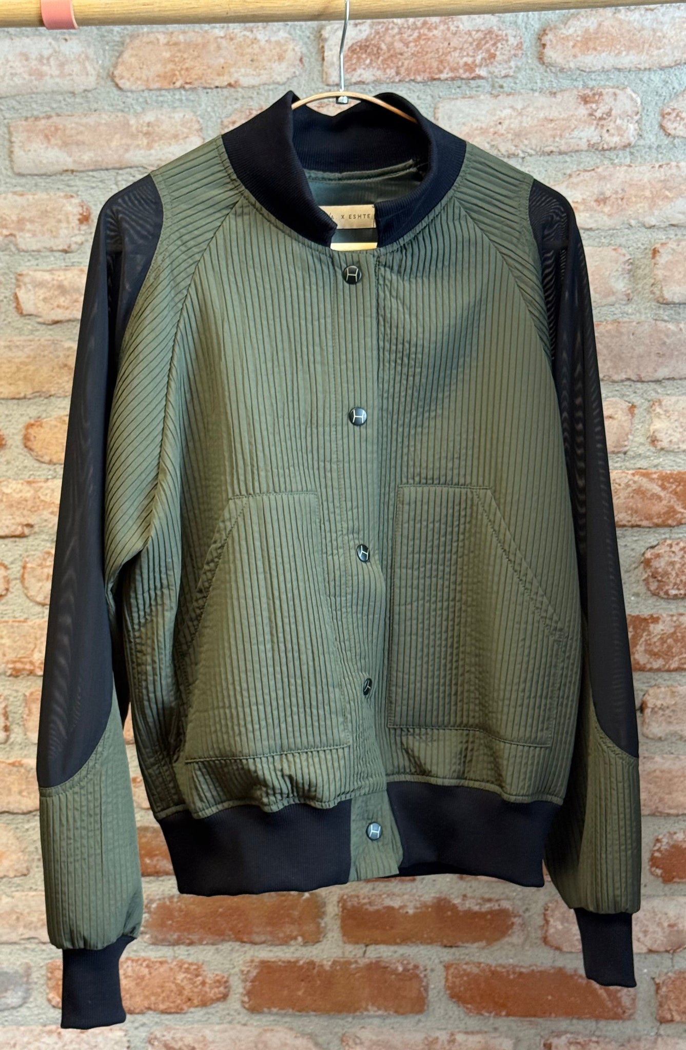 Green and black jacket hanging against a brick wall